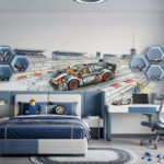 Przestronny pokój z niebiesko-białym tapicerowanym łóżkiem i biurkiem. Na głównej ścianie znajduje się akwarelowa tapeta dla chłopca przedstawiająca tor wyścigowy i sportowe auto zbudowane z klocków. Wnętrze uzupełnia lampa w kształcie kół zębatych, podświetlane heksagonalne półki z zabawkami oraz dywan przypominający tor wyścigowy.