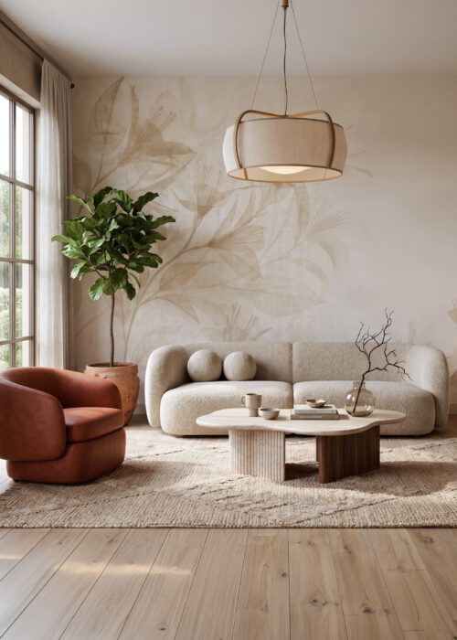Tapeta beżowa w Lilie "Sand Lily" Japandi. Kadr z wnętrza nowoczesnego salonu z widokiem na sofę, fotel i okno. Główna ściana pokryta jest beżową tapetą Sand Lily z subtelnym wzorem botanicznym. Pośrodku znajduje się obła sofa z tkaniny boucle w kolorze owsianki, a obok niej skórzany fotel terakota. Przed sofą stoi stolik kawowy o nieregularnym kształcie z trawertynu i drewna. Pod stopami dywan z juty o ciekawej fakturze. Po lewej stronie duże, wielo-dzielne okno wychodzące na ogród. Nad stolikiem wisi pleciona lampa wisząca. W kompozycji widać również dużą roślinę Fikus Lyrata w terakotowej donicy, nowoczesną konsolę z ceramiką i dekoracje.