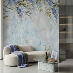 Nowoczesne wnętrze salonu z dużą fototapetą przedstawiającą niebieskie kwiaty wisterii o wyraźnej, malarskiej strukturze. W pokoju znajduje się obła, kremowa sofa typu boucle, fioletowy koc o wysokiej teksturze oraz szklany stolik kawowy na podstawie z lastryko. Całość utrzymana w chłodnej, eleganckiej kolorystyce błękitu i szarości.