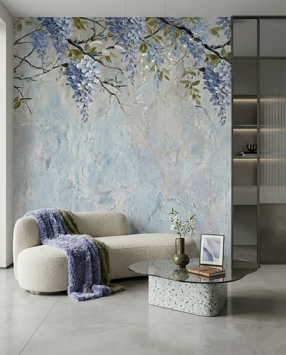 Nowoczesne wnętrze salonu z dużą fototapetą przedstawiającą niebieskie kwiaty wisterii o wyraźnej, malarskiej strukturze. W pokoju znajduje się obła, kremowa sofa typu boucle, fioletowy koc o wysokiej teksturze oraz szklany stolik kawowy na podstawie z lastryko. Całość utrzymana w chłodnej, eleganckiej kolorystyce błękitu i szarości.